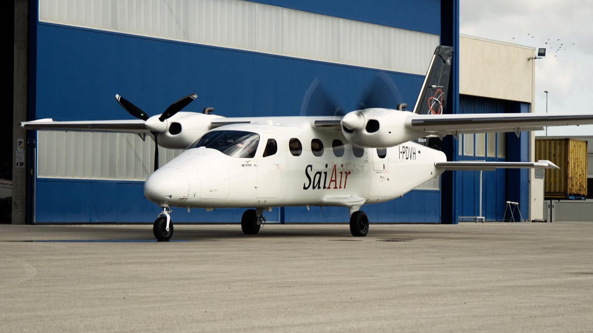 Avión Tecnam P2012 Traveller de SaiAir en plataforma, con motores en marcha frente a un hangar