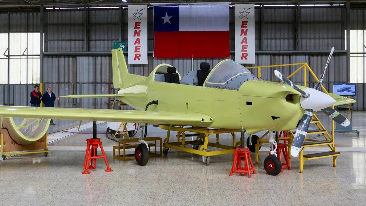 Prototipo del avión T-40 Newén en fase de ensamblaje en el hangar de ENAER con bandera chilena al fondo.