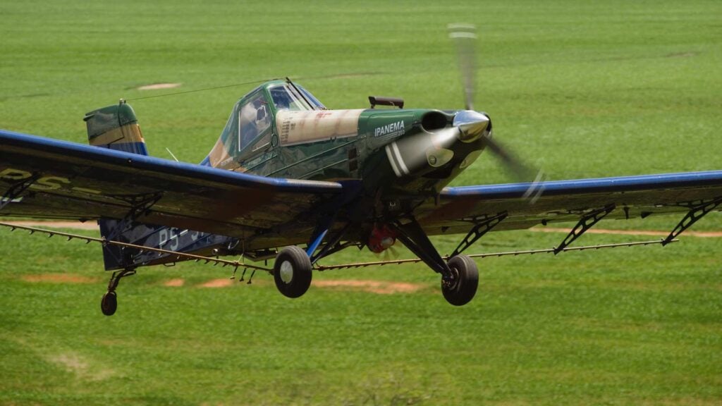 Un avión agrícola Embraer Ipanema 203 propulsado por etanol en pleno vuelo sobre un campo de cultivo en Brasil, ejecutando una pulverización aérea regular