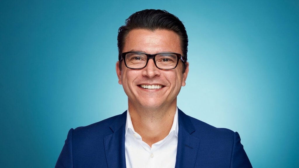 Pascual Álvarez, ejecutivo colombiano, sonriendo de frente con traje azul y gafas, sobre un fondo azul degradado, en su calidad de nuevo Director General de Operaciones de American Airlines para Sudamérica, Centroamérica y el Caribe