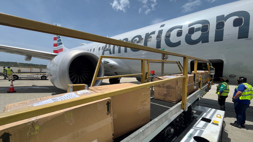 Cajas con suministros de emergencia siendo ingresadas mediante una cinta transportadora a la bodega de carga inferior de un avión Boeing 737 de American Airlines.
