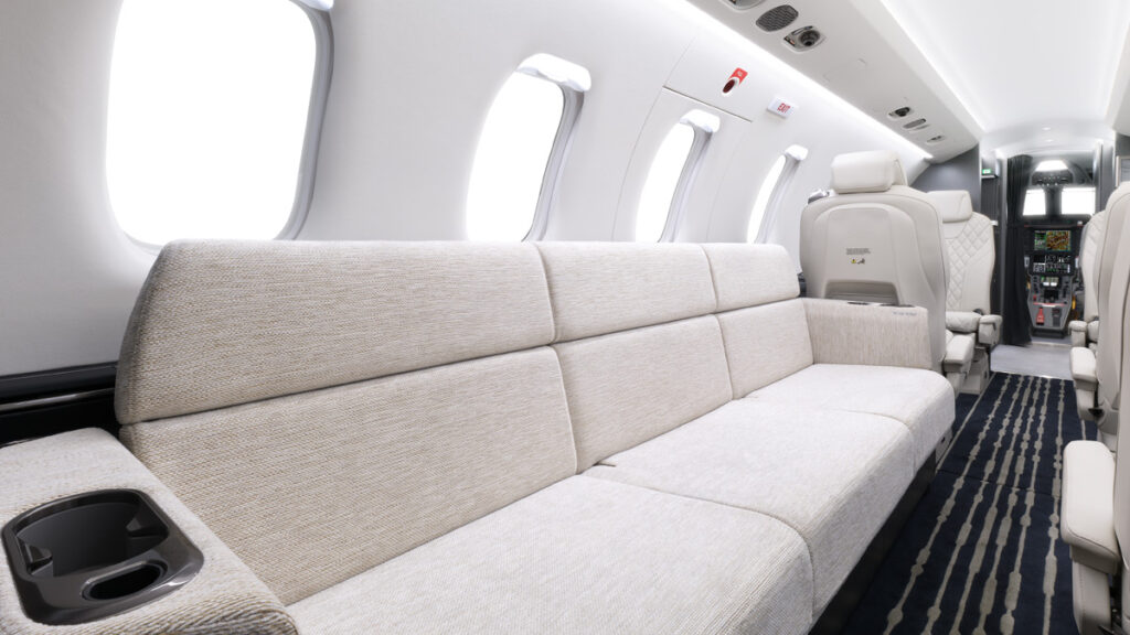 Cabina interior del jet Pilatus PC-24 configurada con un amplio diván lateral tapizado en tonos claros, convertible en cama
