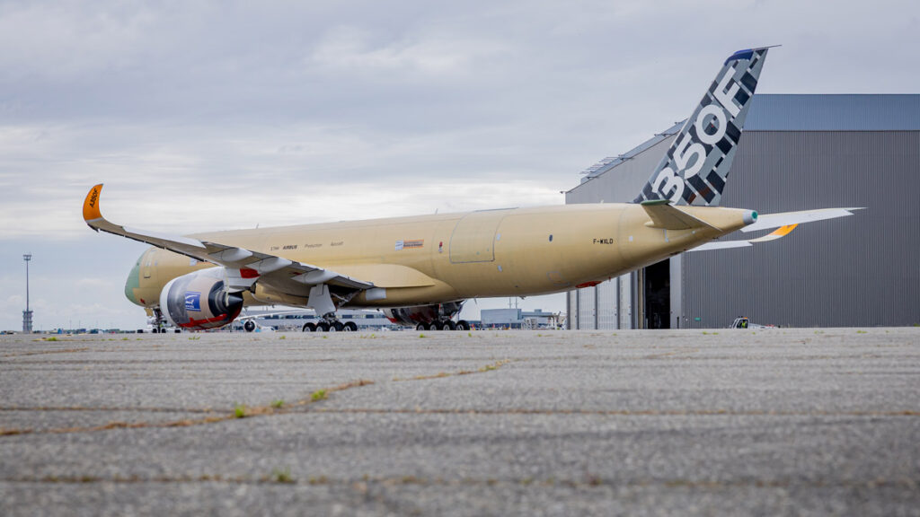 Avión de carga Airbus A350F estacionado en plataforma frente a un hangar, mostrando el diseño final en su estabilizador vertical y winglets.