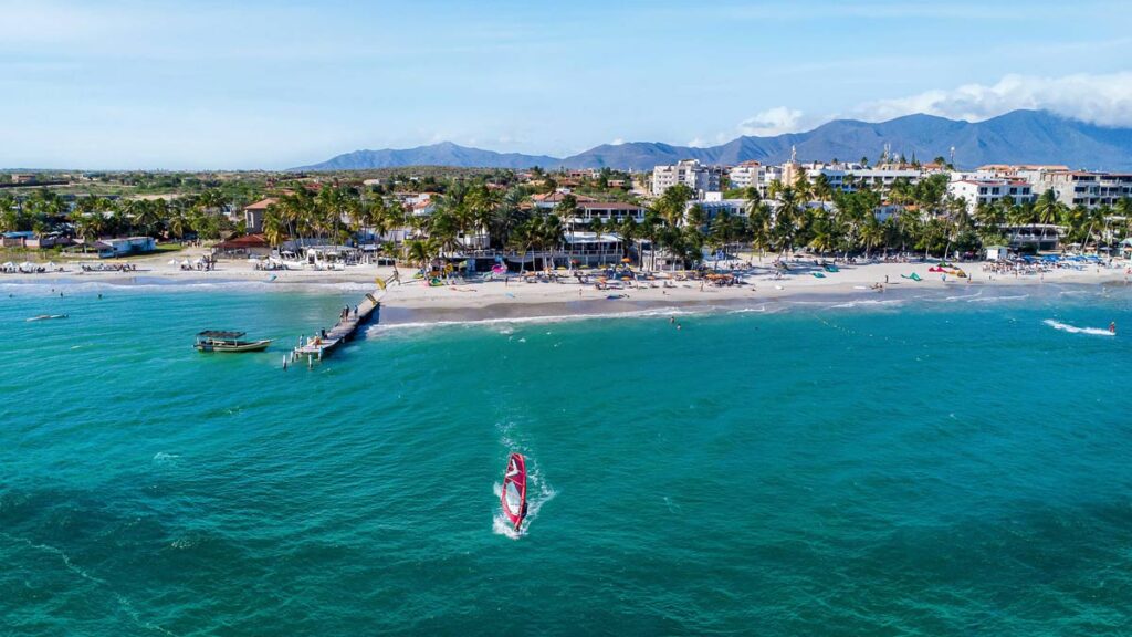 Vista aérea de la playa en la Isla de Margarita con un turista practicando windsurf en aguas turquesas frente a la infraestructura hotelera